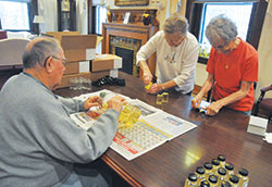 Arnold Feltz, left, Kathleen Feltz and Anna Marie Below, all members of St. Barnabas Parish in Indianapolis, prepare oils on April 8 in the rectory of SS. Peter and Paul Cathedral Parish in Indianapolis. The oils are among those to be blessed at the archdiocesan chrism Mass on April 16 at the cathedral. (Photos by Sean Gallagher)